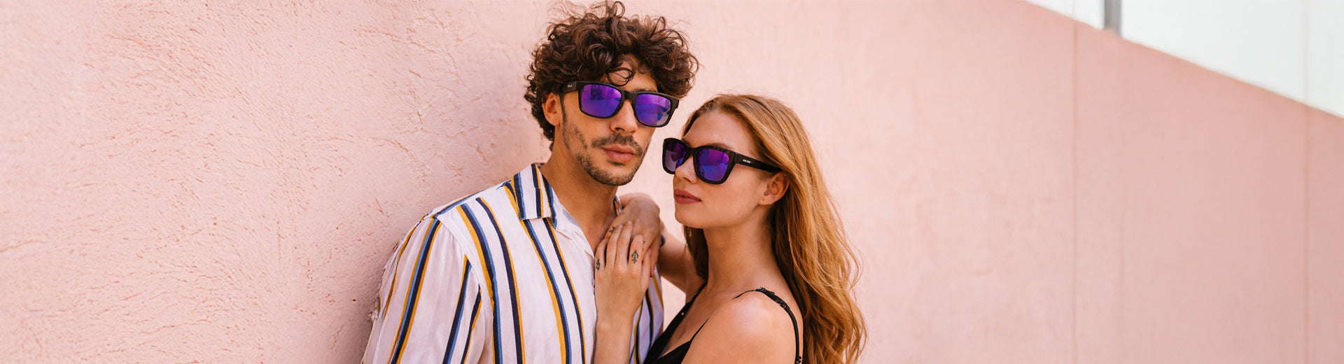 Man and woman wearing sunglasses against a pink wall