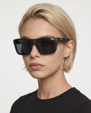 Theo bold wrap sunglasses in Black / Black, black lens on black frame, worn by a woman, front view